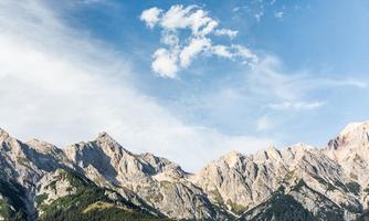 An impressive mountain landscape with steep rocks and green meadows. The sky is blue with a few lightly scattered clouds.