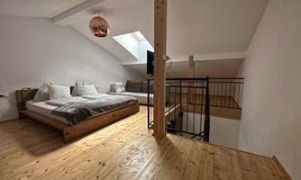 A modern bedroom with wooden floorboards, two beds, and a large window. The decor is bright and inviting, featuring a stylish lamp on the ceiling.