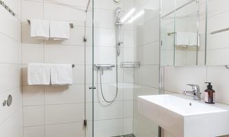 A modern bathroom with a walk-in shower and a sink. The walls are lightly tiled, and there are towels as well as a large mirror.