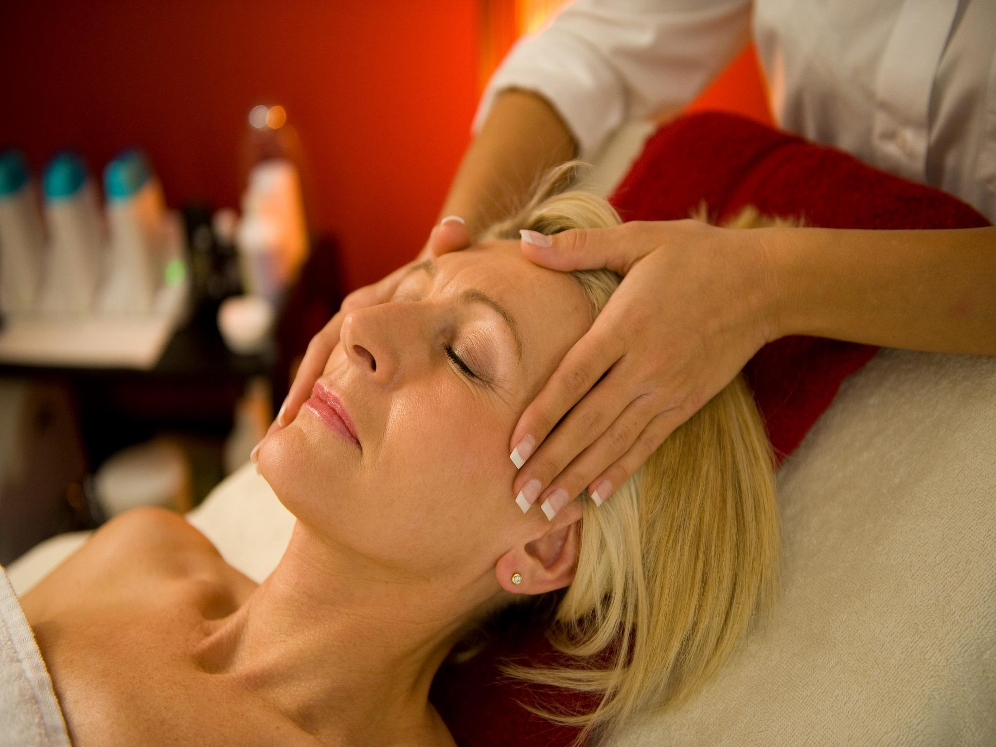 A relaxed woman is receiving a facial massage. The surroundings feel soothing and pleasant.