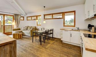A bright and modern apartment with an open kitchen and dining area. The living room is cozy furnished with a sofa and a wooden table.
