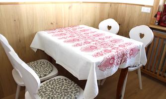 A simple dining area with a table and four chairs. The table is covered with a white tablecloth with a red pattern.
