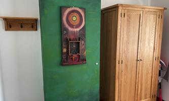 A green wall area with a colorful piece of art in the center. On the right, there is a wood-colored wardrobe.