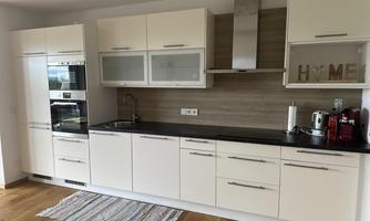 A modern kitchen with white cabinets and a black countertop. The kitchen appliances include a refrigerator, an oven, and various devices.
