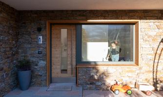 A modern front door with stone cladding. In the window, a person can be seen working inside.