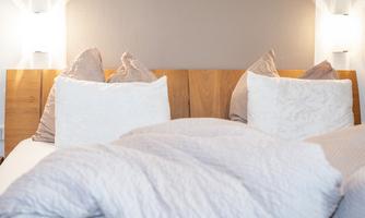 A cozy bedroom with a wooden bed and soft pillows. The gentle lighting creates a relaxed atmosphere.