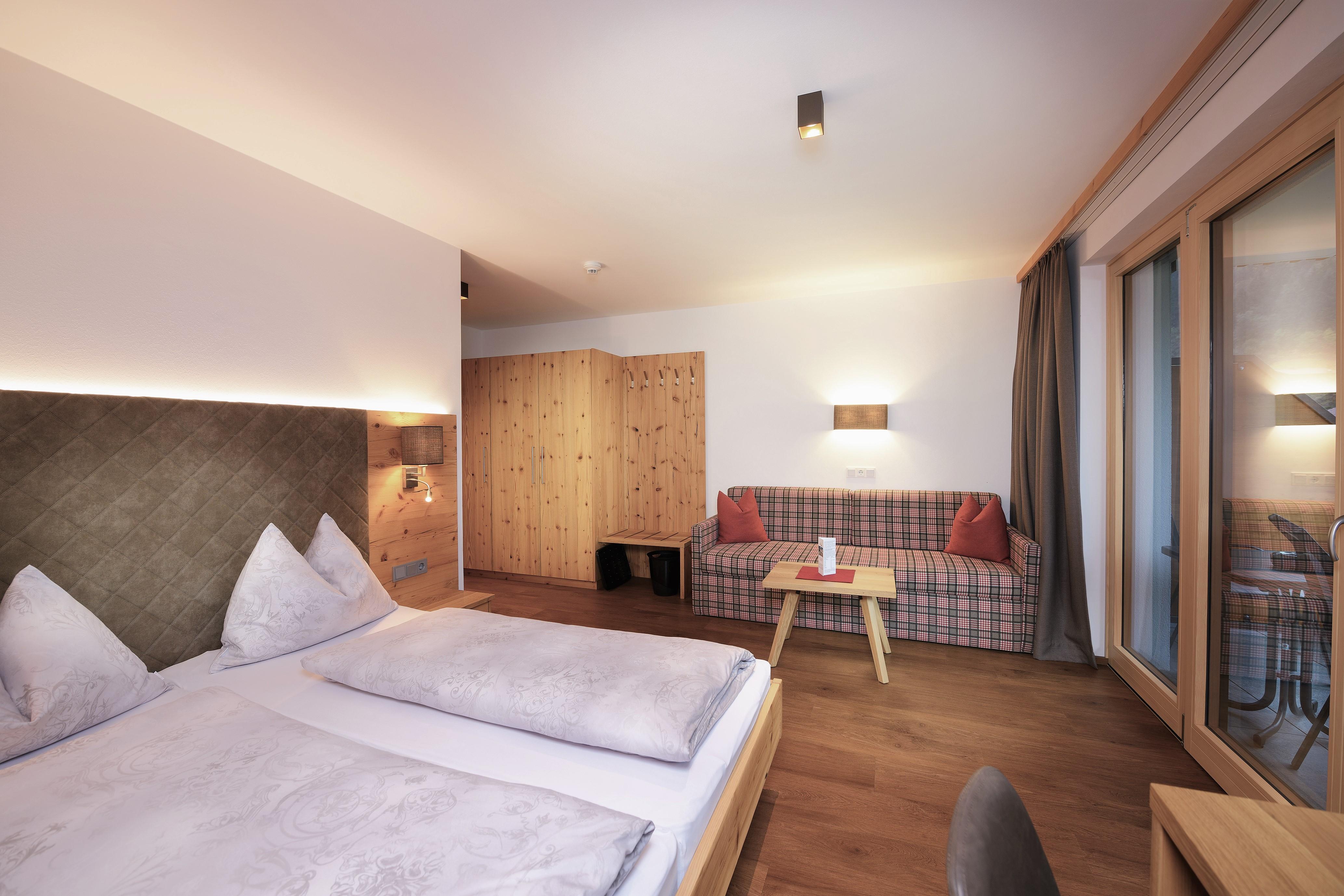 A modern bedroom with two beds and a cozy sitting area. Large windows bring in plenty of daylight and create an inviting atmosphere.
