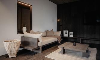 A modern living room with a simple sofa and neutral colors. The room features wooden flooring and understated decor.