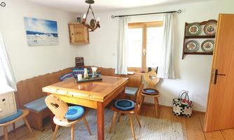 A cozy dining area with a wooden table and chairs. The room is bright and inviting, featuring window views and decorative elements.