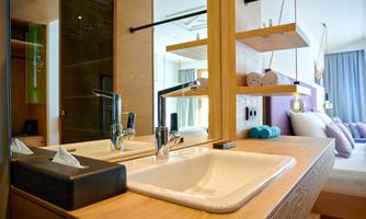A modern bathroom with a clear sink and elegant fixtures. In the background, soft colors and cozy furniture are visible.