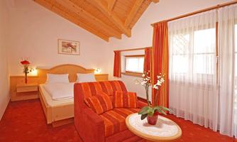 A cozy room with a double bed and a red armchair. Bright curtains and wooden ceilings create an inviting atmosphere.