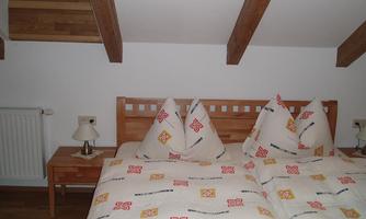 A cozy bedroom with a double bed and two pillows. There is a nightstand and wooden beams on the ceiling.