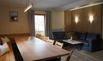 A cozy living space with a long dining table and a comfortable couch. Large windows provide plenty of daylight.