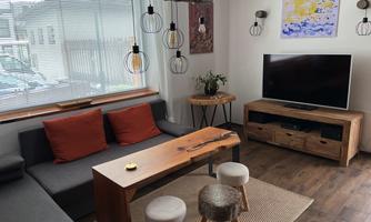 A cozy living space with a gray sofa and wooden furniture. The atmosphere is complemented by modern light sources and colorful artworks on the wall.