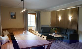 A cozy living space with a long dining table and an L-shaped couch. Large windows provide plenty of daylight and an inviting atmosphere.