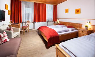 A bright room with two beds and a cozy, modern design. Red curtains and wooden surfaces create an inviting atmosphere.