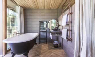 A modern bathroom with a freestanding bathtub and wooden floor. Large windows provide plenty of natural light and an elegant atmosphere.