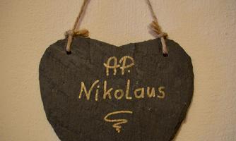 A heart-shaped plaque made of slate with the inscription "AP Nikolaus". It is attached with a string and has a natural, rustic appearance.