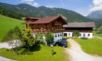 A traditional chalet in the mountains with colorful flowers and green grass. In the background, majestic mountains can be seen.