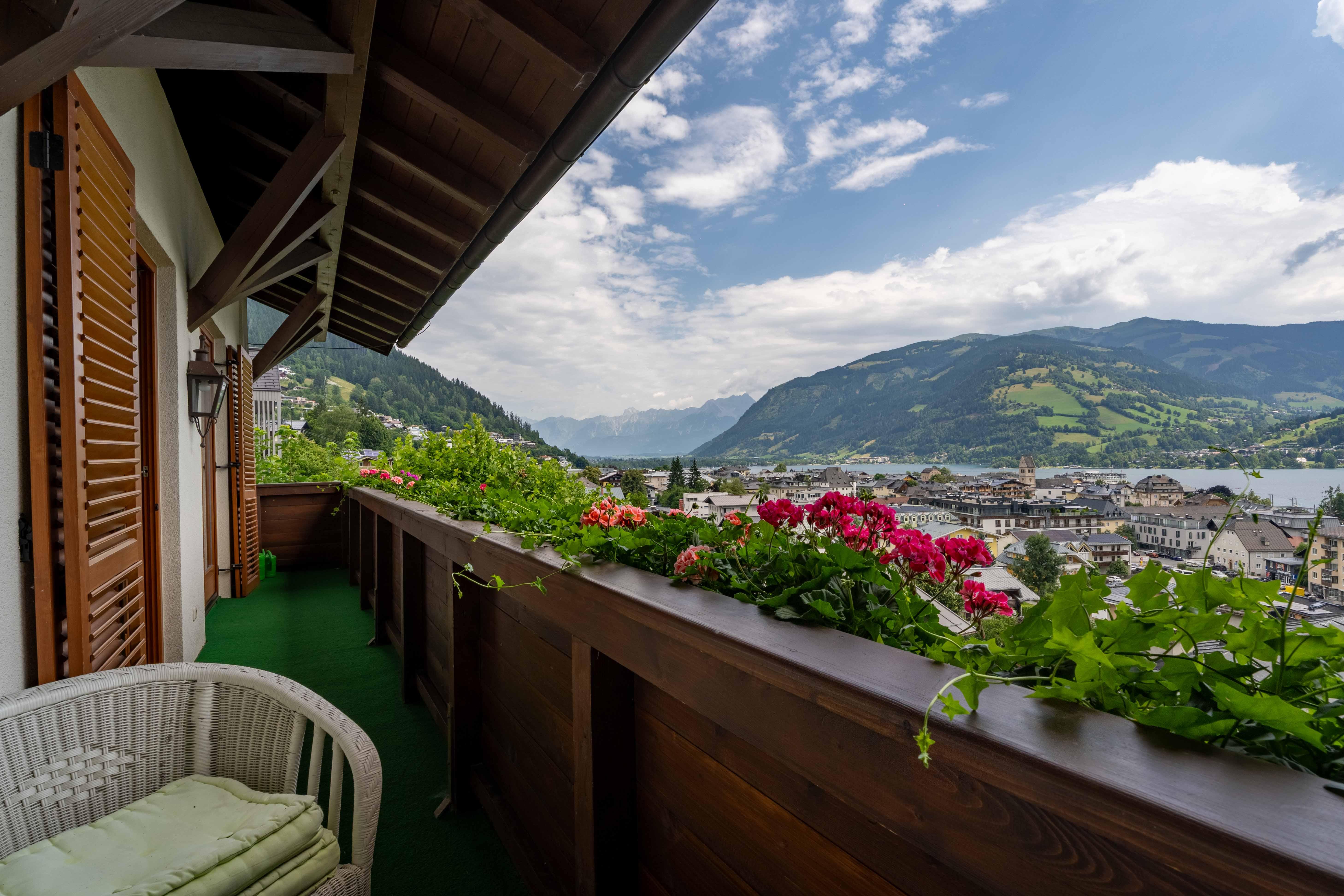 A beautiful balcony with colorful flowers and a view of the mountains and the lake. The sky is clear and the landscape looks peaceful.