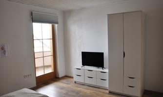 A bright room with a television and a white cupboard. The large sliding door lets in a lot of light.