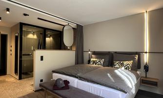 A modern bedroom with a double bed and elegant furnishings. In the background, a bathroom area is visible.
