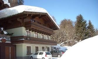 A cozy wooden house in the snow with a large roof. Surrounded by snow-covered trees and clear sky.
