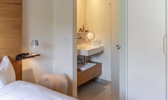 A modern room with a comfortable bed and access to the bathroom. The room has bright walls and an inviting atmosphere.