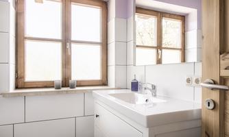 A modern bathroom with a white sink and wooden framed windows. The walls are designed to be bright and welcoming.