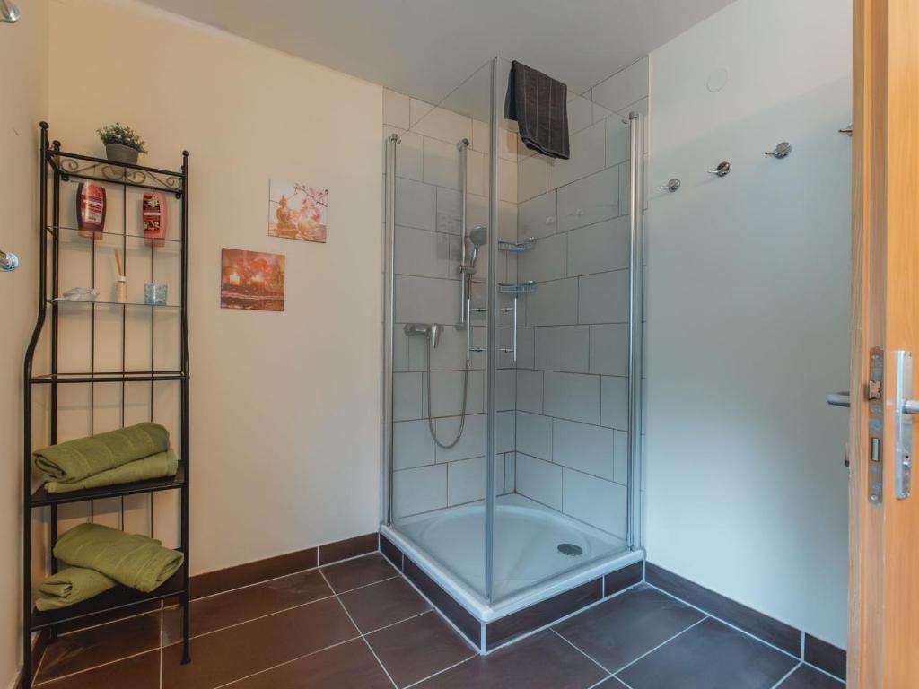 <p>Modern bathroom with a corner glass shower, white tiled walls and dark flooring. Several hooks are mounted on the wall, next to a narrow shelf with towels and decorations.</p>