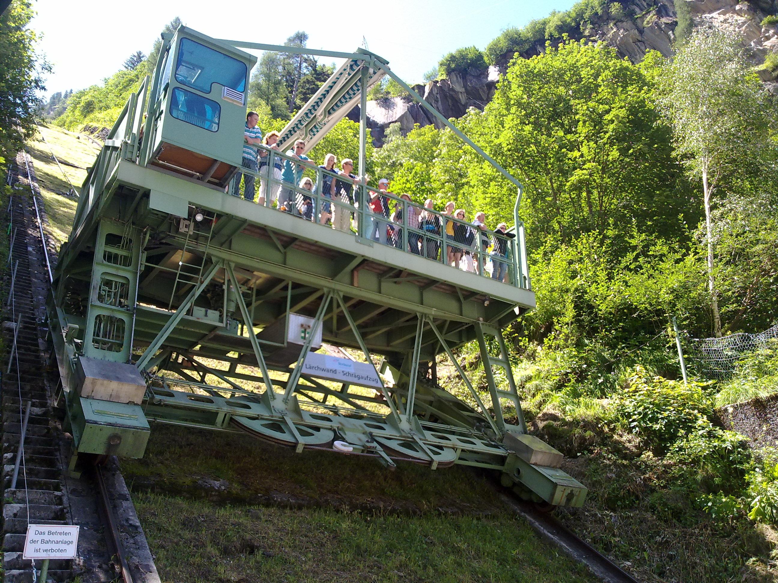 A large funicular railway ascends a slope. Many people are standing on the platform and enjoying the view.