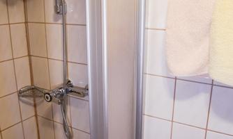 A shower cubicle with tiled walls and a showerhead. A towel hangs next to the shower.