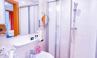 A modern bathroom with a shower and a sink. The walls are tiled in light colors, and there is a large mirror.