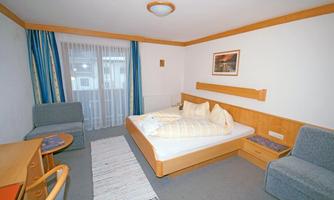 A cozy hotel room with a double bed and a small table. There is a desk, an armchair, and large windows with curtains.