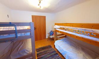 A simple children's room with two bunk beds and a colorful rug. The walls are light, and there is a wooden wardrobe door.