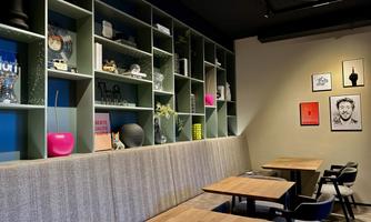 A modern café with minimalist interior and cozy tables. The wall is adorned with shelves and decorative objects as well as artworks.
