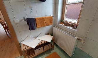 A bright bathroom with white tiles and a wooden shelf. Towels hang on the wall and a relaxing atmosphere is created by the window.