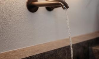 A modern metal faucet that lets water flow into a stylish stone sink. The background is minimalist and well-lit.