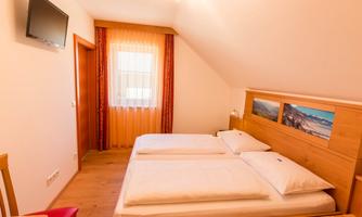 A cozy bedroom with two separate beds and a flat-screen TV. The room has a window with curtains and light-colored walls.