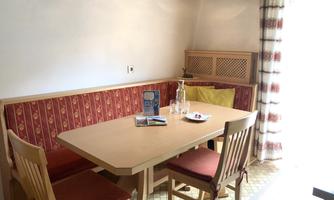 A cozy dining area with a table and chairs. A padded bench is located along the wall, and plenty of natural light streams through the window.