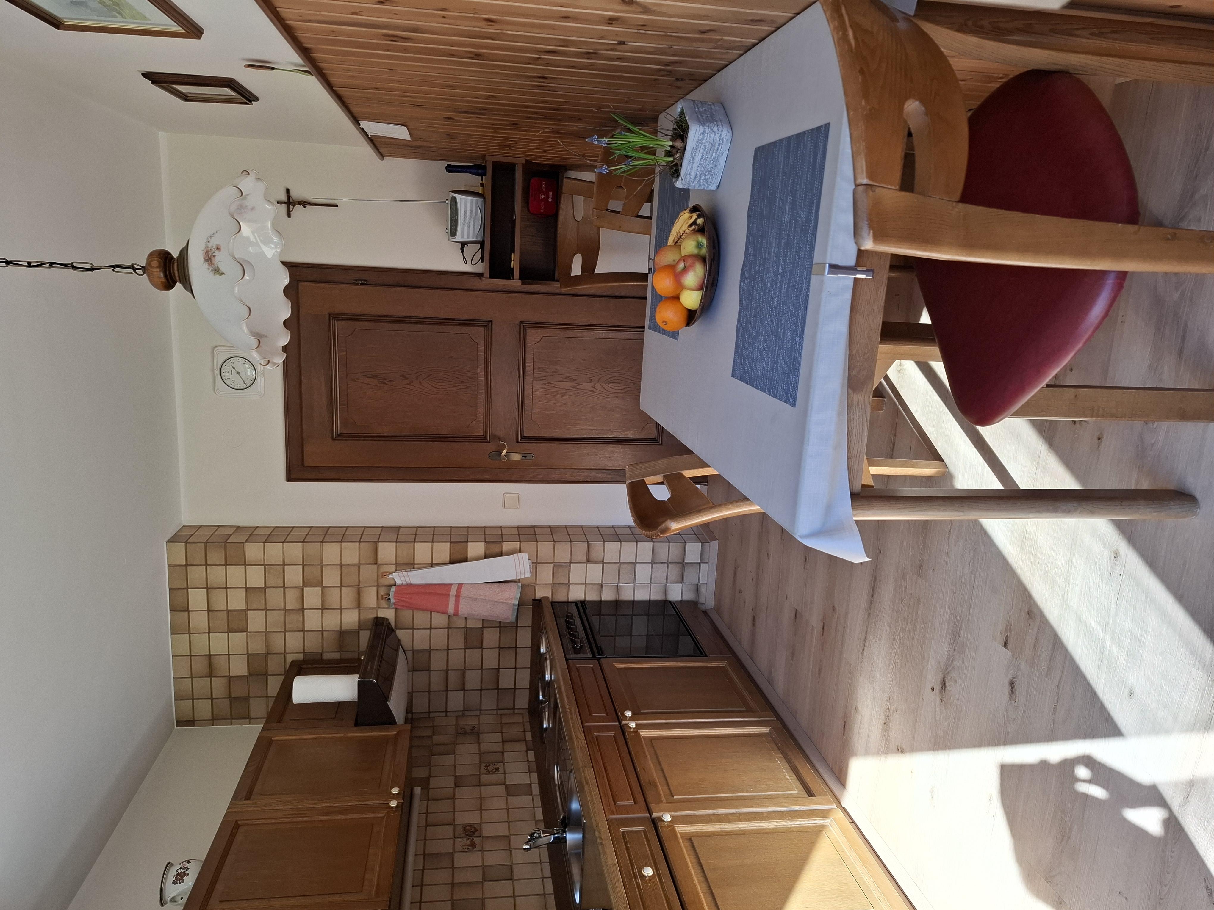 A cozy kitchen with wooden cabinets and a dining table. On the table, there is a bowl of fresh fruit.