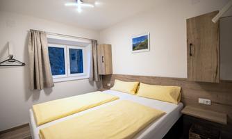 A cozy bedroom with a double bed and yellow bedding. There is a window with curtains and a wooden wall unit.