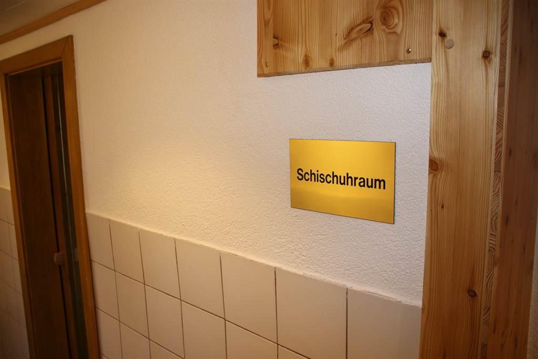 A sign with the inscription "Ski Boot Room" on a wall. The room is simply designed with white tiles and a wooden element.
