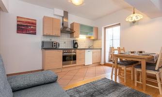 A modern kitchen with wooden cabinets and a dining area. The space is bright and cozy, ideal for shared meals.