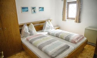 A simple bedroom with two beds and colorful bedspreads. Pictures hang on the walls and there is a window with curtains.