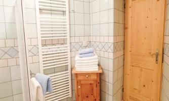 A modern bathroom with white tiles and a wooden door. Clean towels are stacked on a small table.