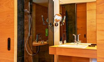 A modern bathroom with wooden paneling and a shower cabin. On the sink shelf, there are toiletries and a mirror.