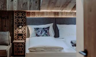 A cozy bedroom with wooden walls and a large window. The bed is inviting and decorated with stylish pillows.