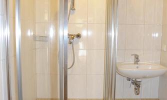 A modern bathroom with a glass shower cabin and a sink. The walls are tiled and the ceiling is made of wood.