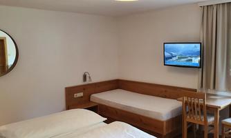 A cozy room with two single beds and a table. A TV hangs on the wall, and there is a window with a view.